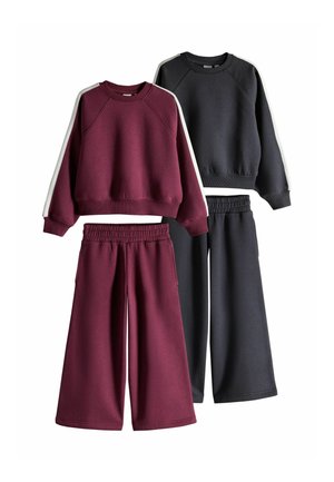 Zwei Sets aus langärmeligen Sweatshirts und weiten Hosen, eines in dunklem Burgunderrot mit weißen Streifen an den Ärmeln, eines in Schwarz mit weißen Streifen an den Ärmeln.