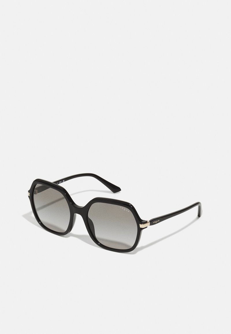 Black oversized sunglasses with gray gradient lenses, angular frame, and gold accents at the hinges. Smooth, glossy texture.