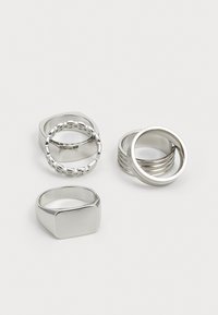 Ensemble de quatre bagues en argent : une rectangulaire, une au design de chaîne bouclée, une de bandes empilées et une lisse et ronde ; finition métallique polie.