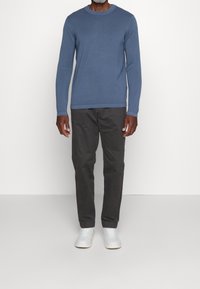 Maglione a maniche lunghe azzurro chiaro con collo rotondo, abbinato a pantaloni grigio scuro e sneakers bianche. Design semplice e texture morbida.