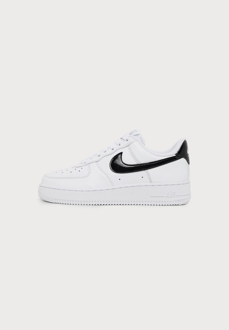 Λευκό χαμηλό sneaker με μαύρο λογότυπο Nike και λεπτομέρεια στη φτέρνα, σχεδιασμό με κορδόνια και διάτρητο μπροστινό μέρος πάνω σε μονόχρωμο φωτεινό φόντο.