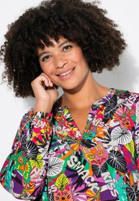 Bunte Bluse mit einer lebhaften Mischung aus floralem und tierischem Druck in Grün, Pink, Gelb und Lila, mit V-Ausschnitt und langen Ärmeln.