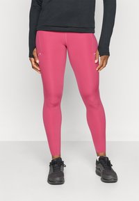 Tætsiddende pink leggings lavet af strækbart materiale, der har en glat overflade og sidelommer, parret med sorte træningssko.