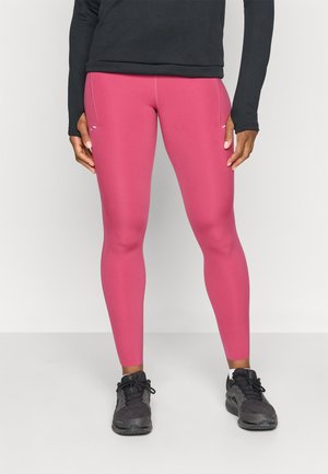 Tætsiddende pink leggings lavet af strækbart materiale, der har en glat overflade og sidelommer, parret med sorte træningssko.