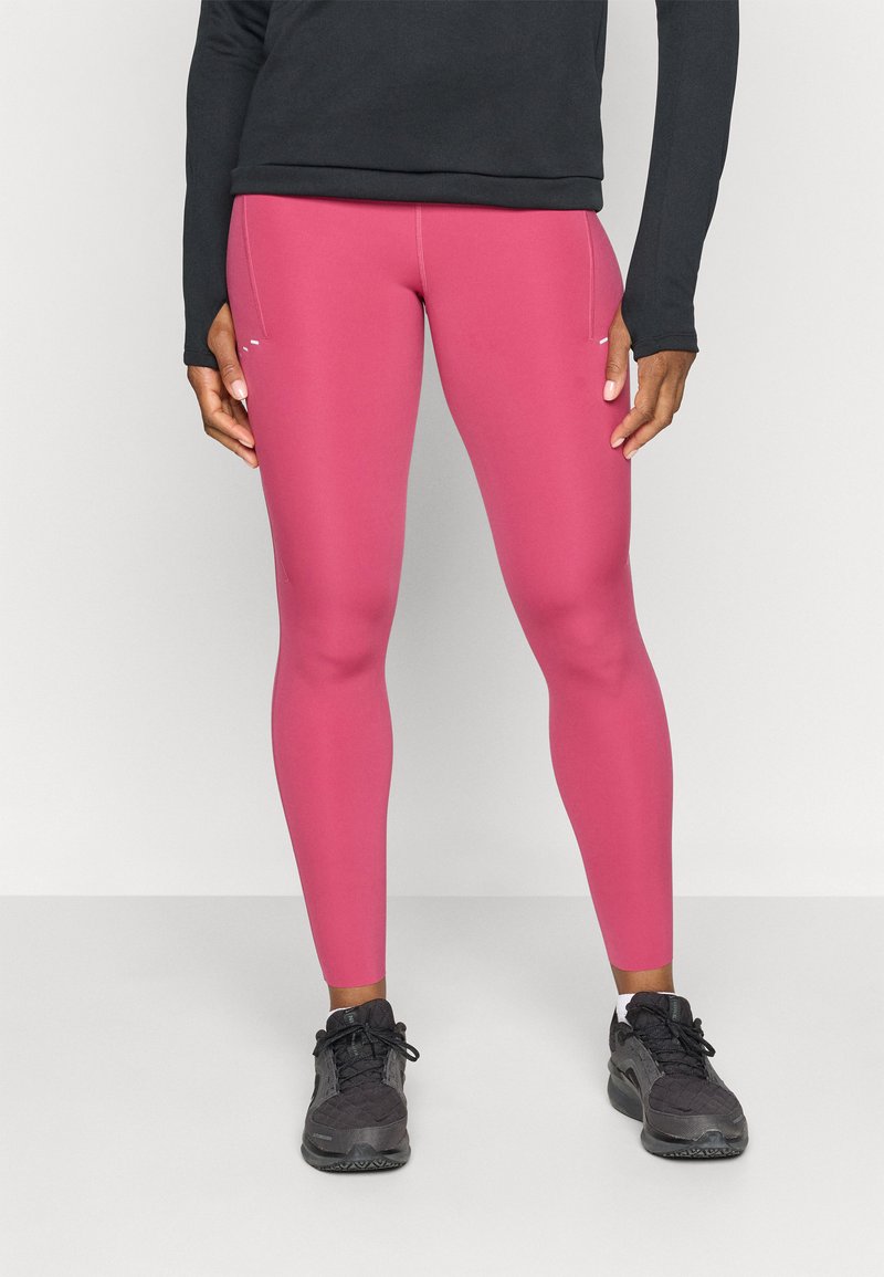 Tætsiddende pink leggings lavet af strækbart materiale, der har en glat overflade og sidelommer, parret med sorte træningssko.
