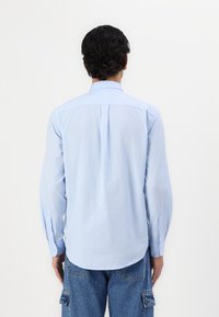 Camisa de botones de manga larga en azul claro, con un pliegue en la parte posterior, dobladillo redondeado y puños con botones, hecha de una tela suave y ligera.