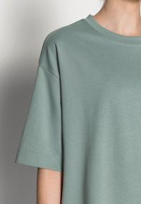 Zelené oversized tričko z měkkého materiálu, s kulatým výstřihem a krátkými rukávy s čistými švy.