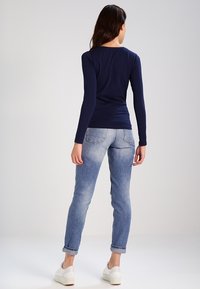 Mörkblå långärmad topp i kombination med ljusblå smala jeans och vita sneakers. Slät tyg med en figurnära design och uppvikta ärmar.