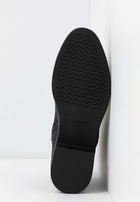 Suela de zapato negra con patrón de olas texturizado, etiquetada "ANNA FIELD" y tamaño "38". Presenta una forma plana y redondeada, y un material resistente.