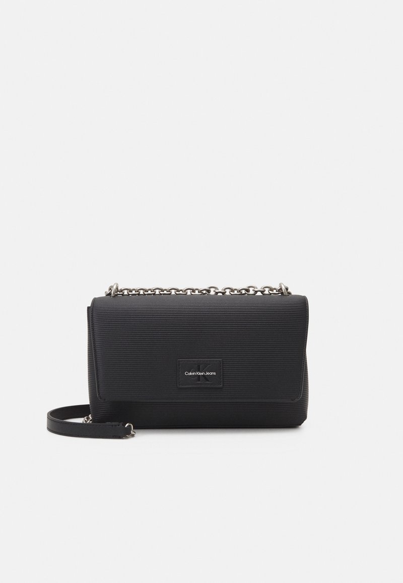 Svart rektangulär handväska med ribbad textur, rem av metallkedja och en logotypmärket framtill. Har en viks över klaffstängning.