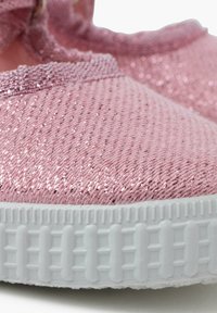 Rosa strukturierte Slippers mit glitzerndem Finish, ausgestattet mit einer weißen Gummisohle mit gemustertem Profil. Hergestellt aus weichem und flexiblem Material.