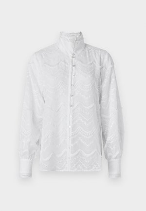 Hvit bluse med høy krage, lange ermer og knappestolpe. Har teksturerte bølgete mønstre og blonder detaljer ved mansjettene.