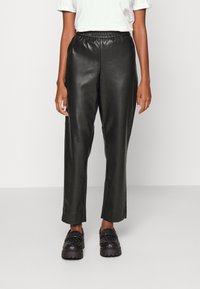 Black faux leather pants with an elastic waistband, straight-leg cut, and smooth texture, paired with chunky black platform shoes.