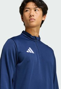 Ναυτικό μπλε αθλητική μπλούζα με φερμουάρ έως το ένα τέταρτο, φτιαγμένη από λείο συνθετικό ύφασμα, με λευκό λογότυπο Adidas στο αριστερό στήθος.