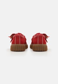 Zapatos de ante rojo con un aspecto texturizado, que cuentan con suelas acanaladas marrones y costuras blancas en contraste a lo largo de la parte trasera y los lados.