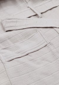 Šviesiai pilkas tekstūruotas audinys su zigzago raštu ir subtiliomis juostelėmis, papildytas viena kišene ir minkštu kaklaraiščio uždarymu.