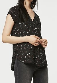 Blouse noire à manches courtes avec un décolleté en V, ornée d'un motif abstrait coloré de petites formes en rouge, blanc et bleu. Tissu léger, coupe ample.