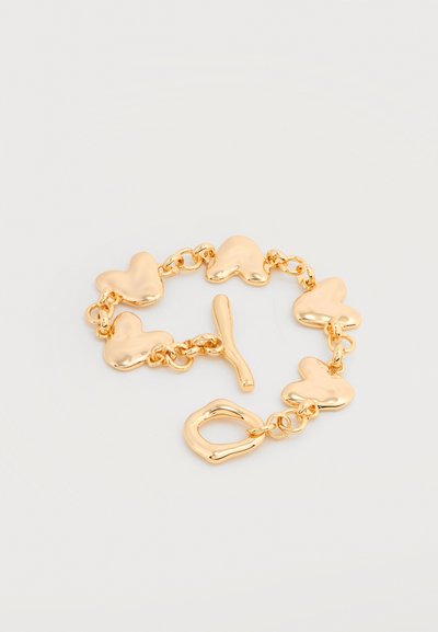 Χρυσό βραχιόλι με πέντε συνδεδεμένους συνδέσμους σε σχήμα καρδιάς και κούμπωμα τύπου toggle σε φωτεινό φόντο.