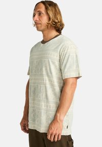 Camisa de manga corta de color verde claro con un cuello acanalado marrón, que presenta un diseño geométrico y detalle en las costuras laterales.