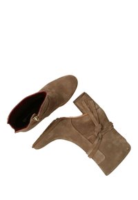 Bottines en daim marron avec fermeture éclair sur le côté, doublure intérieure rouge et détail en nœud avec des sangles d'un côté. Talon plat.