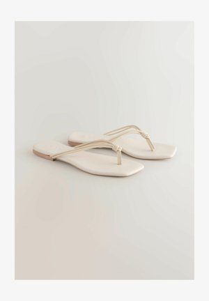 Platte sandalen met een vierkante teenvorm, gemaakt van zacht, lichtbeige materiaal. Twee dunne banden kruisen elkaar bij de tenen, met een geknoopte accent.