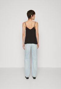 Black camisole with thin straps, v-back design, lightweight fabric. Paired with light blue high-waisted jeans, relaxed fit, straight legs.