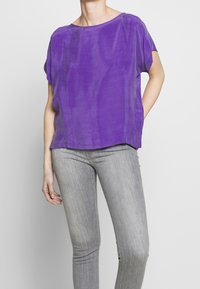 Lila kortärmad topp i lätt tyg, med rund halsringning och avslappnad passform, i kombination med grå tajta jeans.