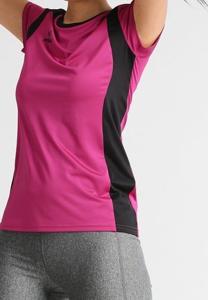 Close-up of a person wearing a pink and black sports shirt and gray leggings, raising arms above the head against a plain background.
