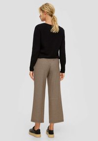 Zwarte gebreide trui, bruine geruite wijde broek en zwarte platform sneakers. Achteraanzicht, natuurlijk haar in een staart gestyled.