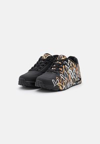 Sneakers neri con una parte superiore testurizzata, caratterizzati da un audace motivo astratto arancione e bianco sui lati e una suola nera robusta.
