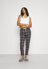 White tank top, navy plaid pants with red and white lines, and gray fuzzy slippers. Pants feature an elastic waistband with drawstring.