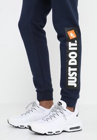 Marinblå joggers med en svart och vit "JUST DO IT." grafik längs sidan, tillsammans med vita sneakers med svarta accenter och texturerade snören.