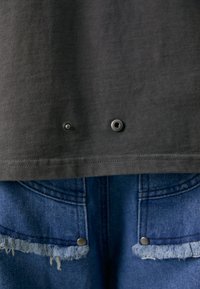 Dark grey cotton shirt with snaps at the hem, worn over blue denim shorts featuring frayed edges and metal button accents.