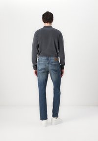 Šedé tričko s dlouhým rukávem, modré džínové kalhoty s kapsami na zadní straně a logovou nášivkou, a bílé tenisky. Jednoduchý, moderní design a přiléhavý střih.