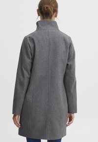 Manteau en mélange de laine gris avec un col haut, coupe droite et manches longues. Présente des lignes épurées et des détails de couture subtils.