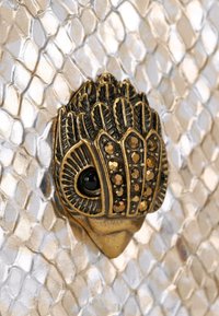 Superficie texturizzata di pelle di serpente metallizzata oro e argento con un accento di hardware dettagliato di colore bronzo adornato con gemme simili a pietre nere e marroni.