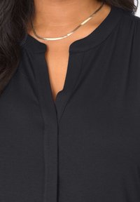 Czarna bluzka z krótkim rękawem, okrągłym kołnierzykiem i bezguzikowym zapięciem. Miękka, gładka tekstura i lekki materiał. Prosty, estetyczny design.