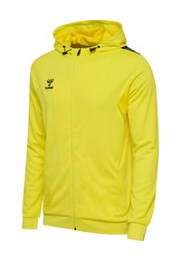 Gul hættejakke med et struktureret mønster, sort logo og detaljer, lynlås lukning og sidelommer. Glat stof, sporty design.