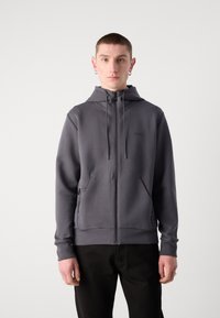 Sudadera con cremallera gris hecha de una tela suave, con capucha, cordones, dos bolsillos laterales y un pequeño logo en el pecho.