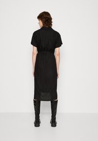 Abito camicia nero midi con maniche corte, dotato di una cintura in vita, taglio dritto e pannello posteriore leggermente trasparente.