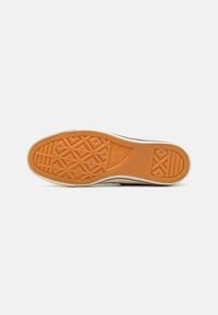 Pohja matalapohjaisten tennareiden, jossa on oranssi kumipohja, johon on merkitty geometrisia kuvioita ja "Converse All Star" -logo keskellä.