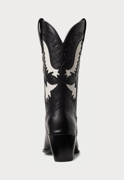 Musta-valge nahast cowboy saabas terava varbaga, väljendunud õmbluse detailidega ja plokk-kandiga. Disain sisaldab keerulisi mustreid võllil.