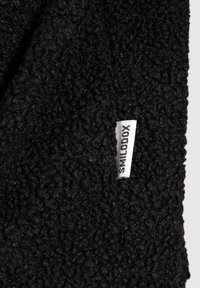 Svart fleece-tyg med en texturerad yta. En liten vit etikett med "SMILODOX" är synlig, sydd längs kanten.