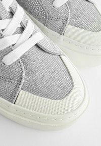 Silver sneakers med en texturerad ovandel, med en glittrig finish, vita snören och en vit gummisula med en mönstrad tåsko.
