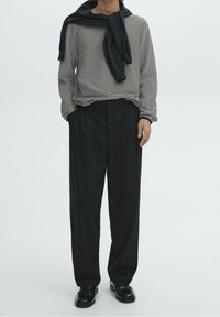 Camicia a maniche lunghe a righe bianche e nere, abbinata a pantaloni neri plissettati. Una sciarpa scura è appoggiata sulla camicia, aggiungendo texture all'outfit.