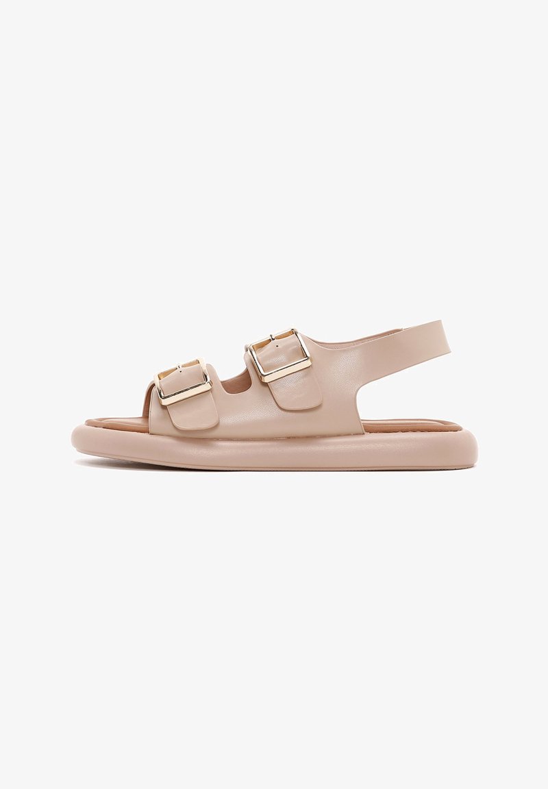 Beige Sandale mit zwei Schnallen, offener Zehenbereich, gepolstertem Fußbett und flexibler Sohle. Glatte Textur mit minimalistischer Optik.