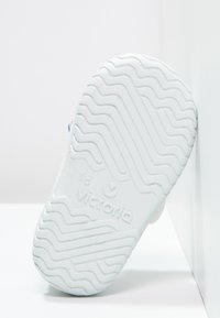 Suela de zapato de goma blanca con patrón de banda ondulada, grabada con "18" y "Victoria". Textura suave, bordes redondeados y diseño minimalista.