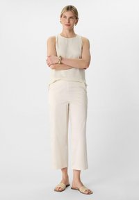 Beige ärmelloses Oberteil, cremefarbene weit geschnittene Hose und gewebte Rutschsandalen. Glatter Stoff, lockere Passform, schlichtes Design und helle Farben.