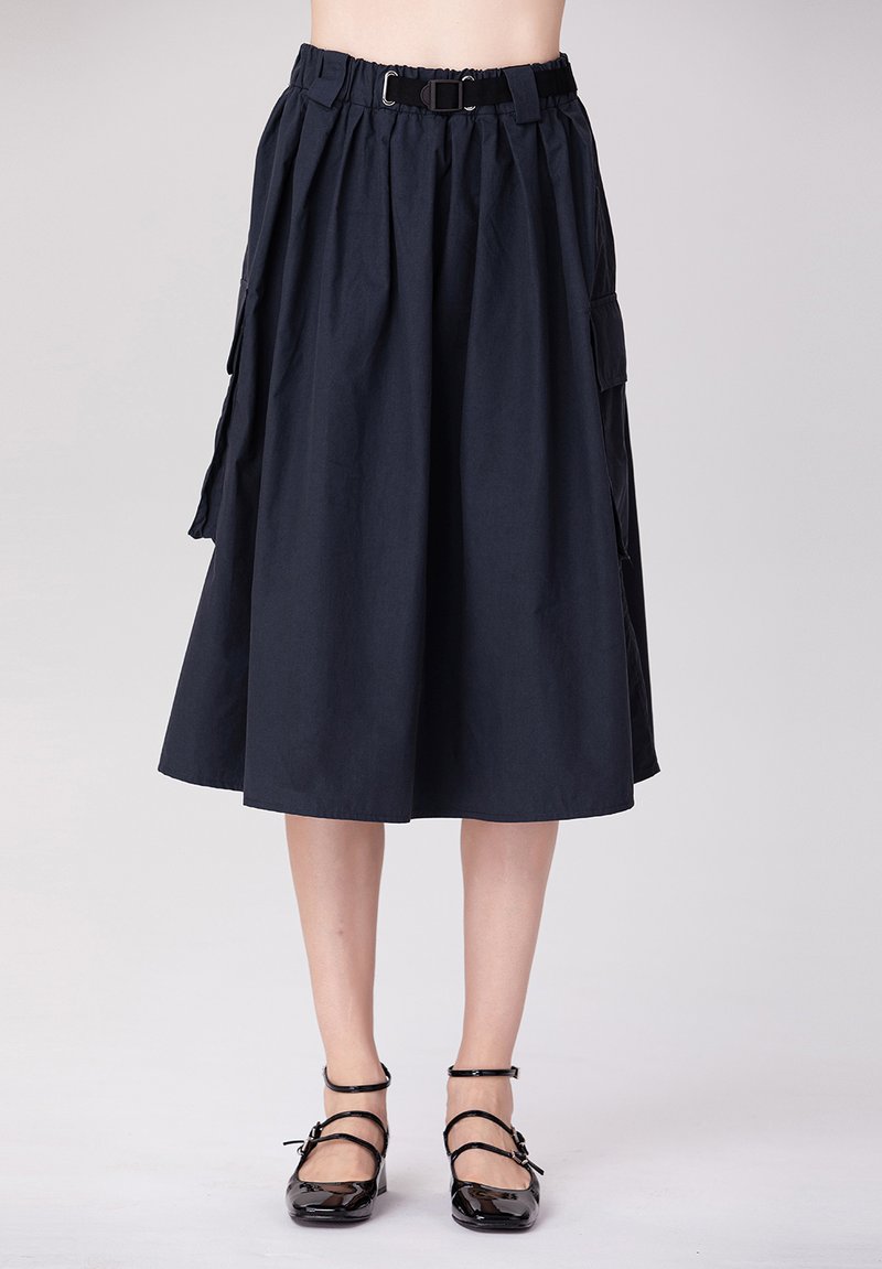 Jupe midi bleu marine en mélange de coton avec des plis, une ceinture ajustable et des poches latérales. Assortie avec des chaussures plates noires à fines lanières.