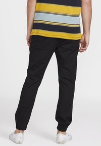 Pantalones negros con puños elásticos combinados con una camisa a rayas multicolor en amarillo, azul marino y azul claro, que presenta un corte relajado y un diseño sencillo.